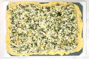 Spinach artichoke filling on top of the dough, ready to roll