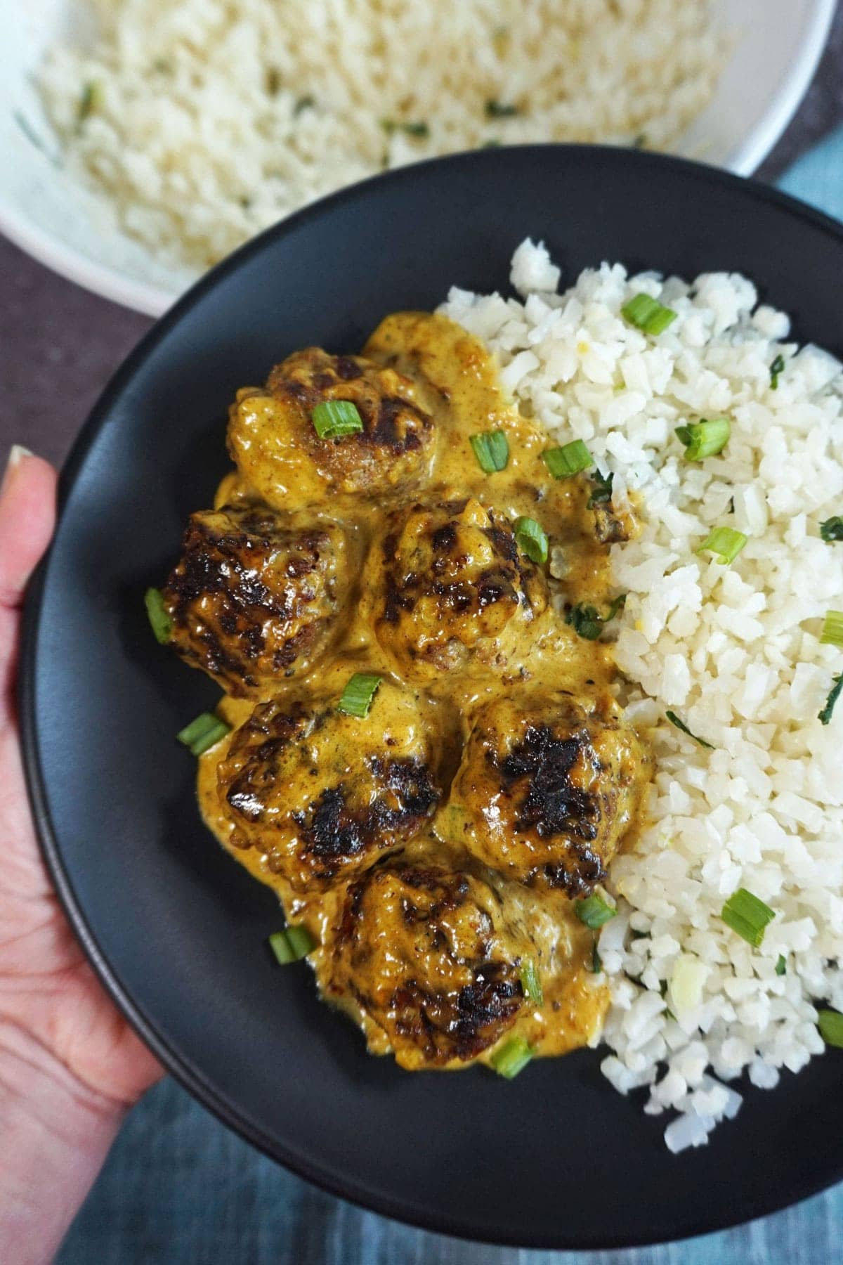 Plate of Keto Swedish Meatballs with Turmeric, a side of cauliflower rice, and topped with fresh green onions