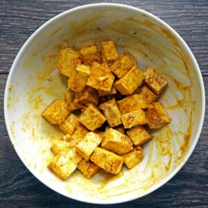 Cubed tofu in a bowl mixed with turmeric and spices