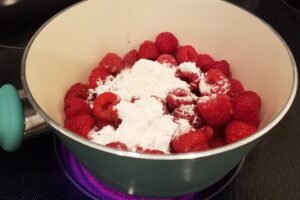 Fresh raspberries and powdered erythritol in a pot over the stove