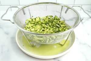 Shredded zucchini in a colander over a plate