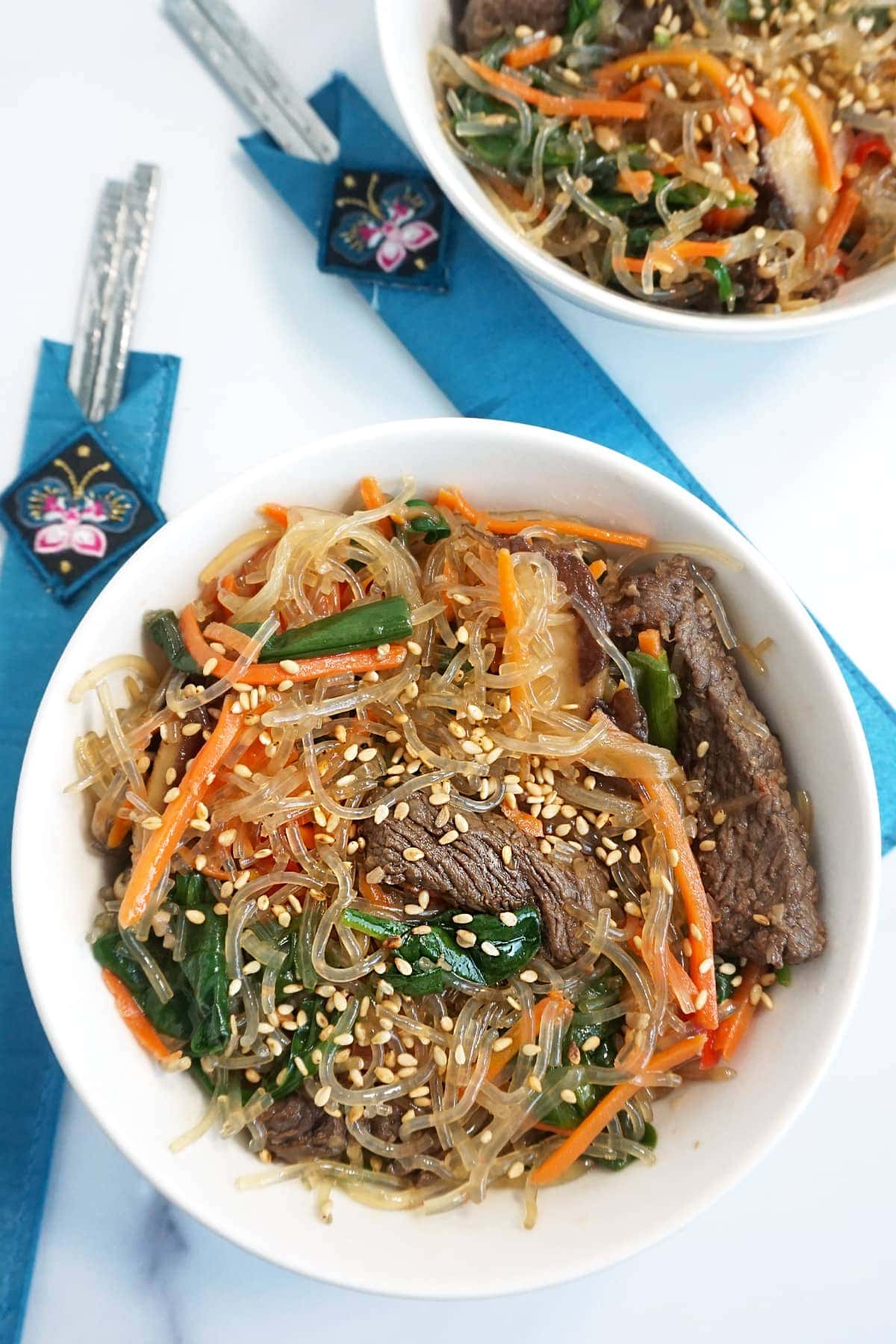 Two bowls of japchae with metal chopsticks on the side