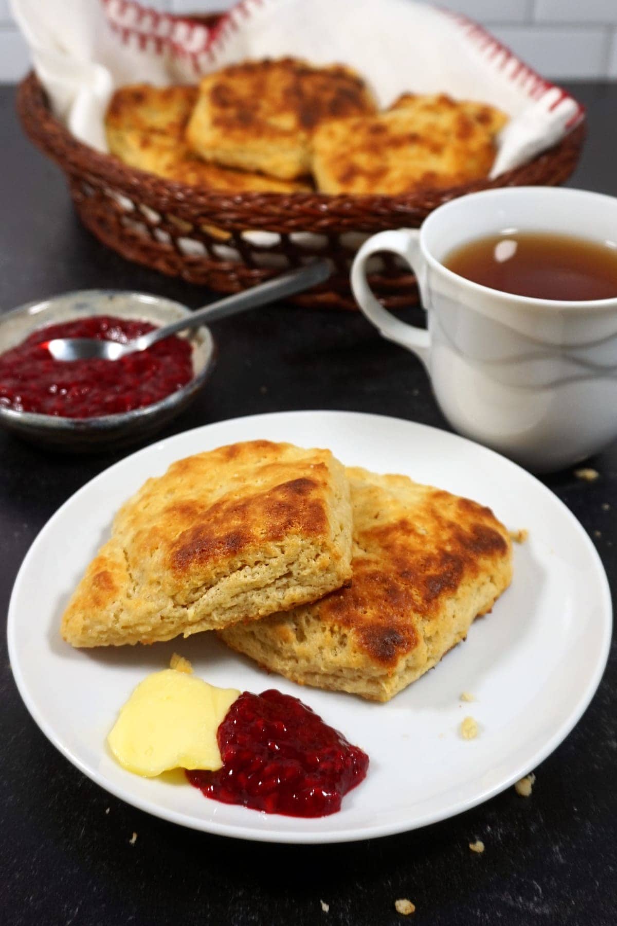 King Arthur biscuits on a plate with raspberry jam, butter, and a cup of tea