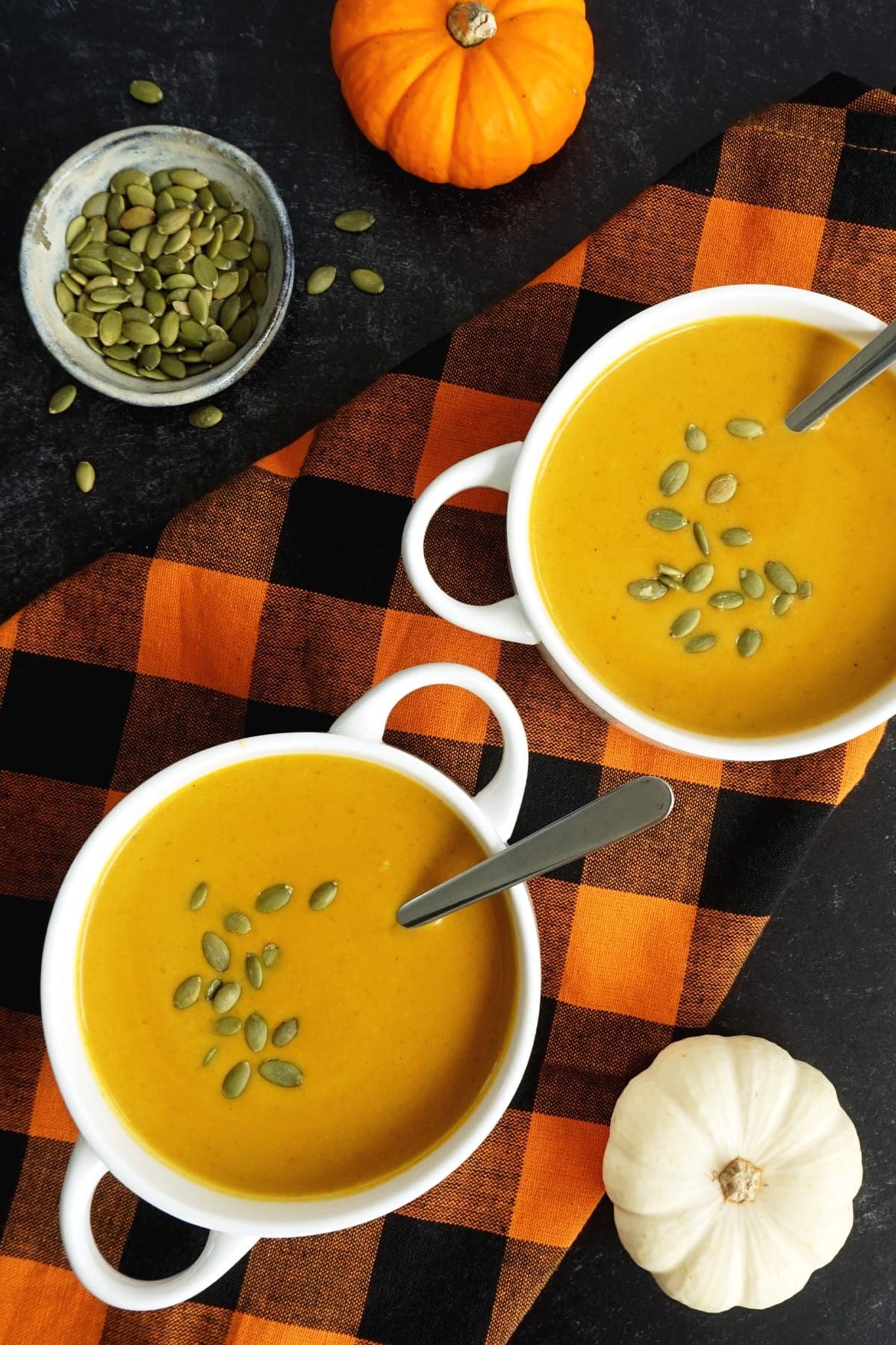Two bowls of savory pumpkin soup with pumpkin seeds on the side