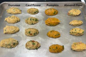 Sheet pan with uncooked bolinhos in 4 rows, labeled: hummus, cauliflower, pumpkin and almond flour