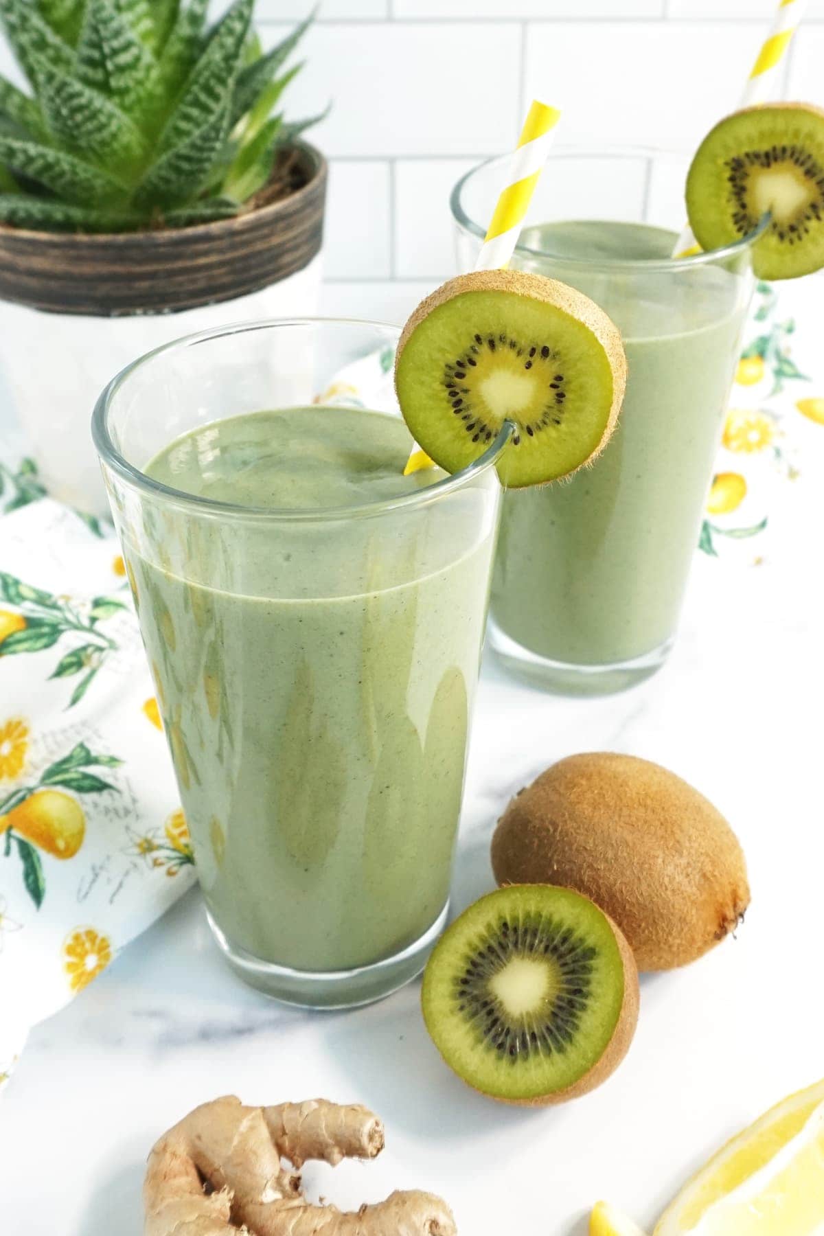 Two cups of Green Detox Smoothie with ginger, kiwi and a yellow straw