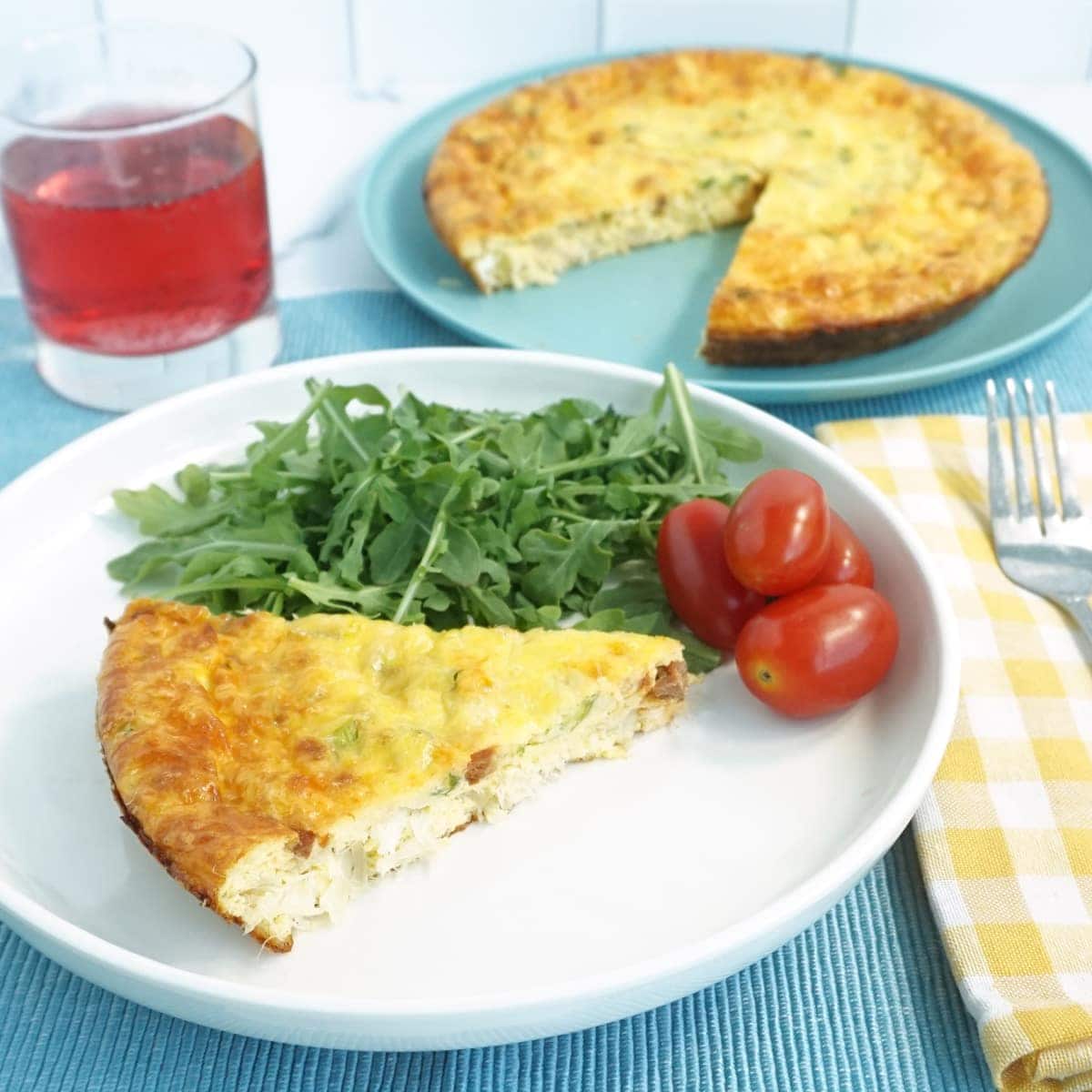 Plate of quiche with arugula and tomato on the side