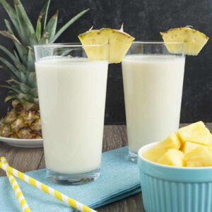 Two cups of pina colada smoothie with a slice of pineapple on top