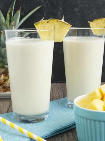Two cups of pina colada smoothie with a slice of pineapple on top